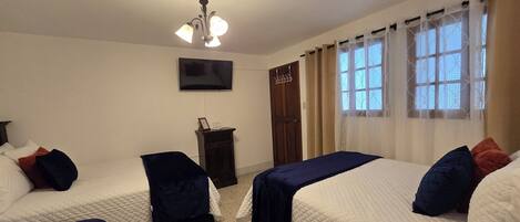 A hotel room with two beds, a TV mounted on the wall, a small cabinet, and a door with a coat rack.