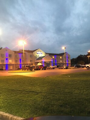 Um hotel com vários andares, estacionamento e uma área gramada na frente.