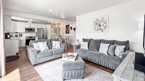 A modern living room with two grey sofas, a coffee table, and a dining area with a chandelier. - 5BR 2BA - Northglenn Bungalow, Family-Friendly Stay Near Denver & Boulder (Northglenn)