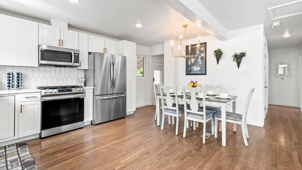 A modern kitchen with white cabinetry, stainless steel appliances, and a dining area with a table and chairs. - 5BR 2BA - Northglenn Bungalow, Family-Friendly Stay Near Denver & Boulder (Northglenn)