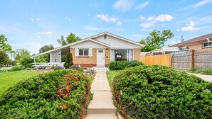 A single-story house with a front porch, a visible garage door, and a well-maintained lawn with trimmed bushes. - 5BR 2BA - Northglenn Bungalow, Family-Friendly Stay Near Denver & Boulder (Northglenn)