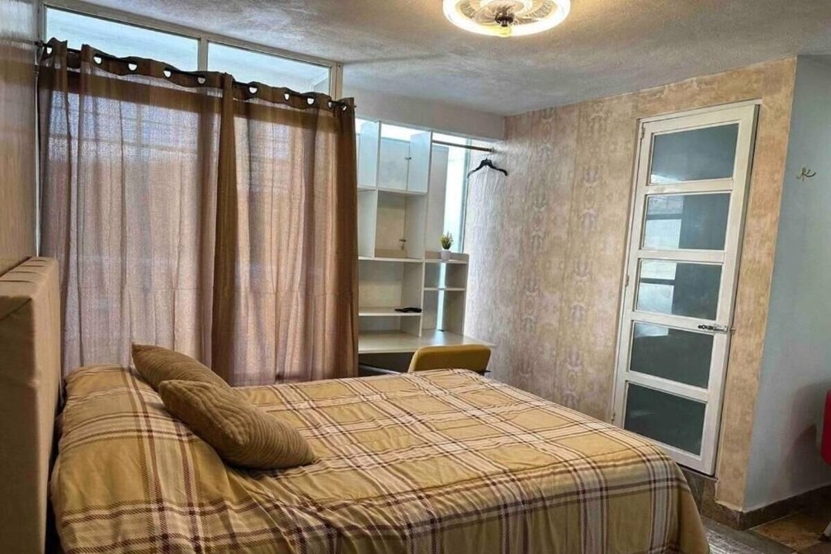 A bedroom with a bed, curtains, a desk, and a wardrobe.