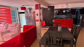 A modern living room with a red sofa, a dining table with chairs, and a kitchen area visible through an open door. - Hospedaje Casa Vazquez  (Pachuca)