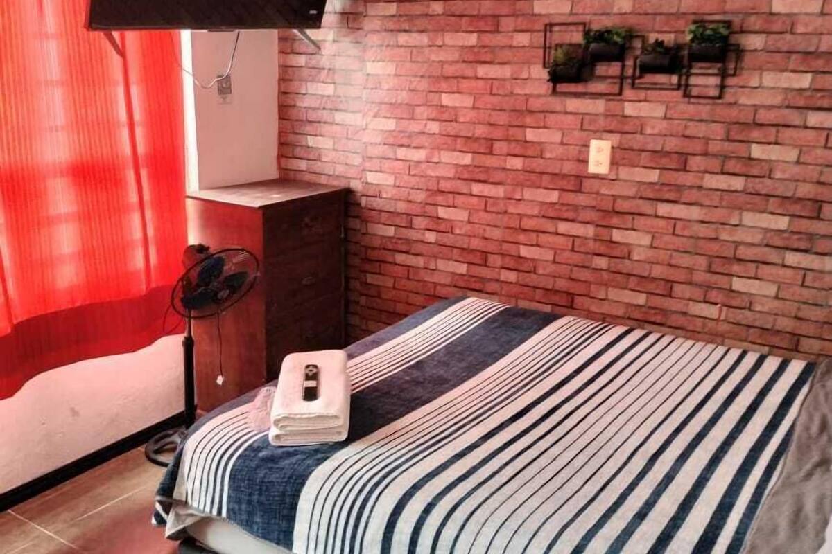 A bedroom with a brick wall, a bed with striped bedding, a TV mounted on the wall, and a red curtain.