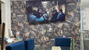 A conference room with a large flat-screen TV mounted on a textured wall, blue upholstered chairs, and a glass table. - Hospedaje Casa Vazquez  (Pachuca)