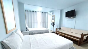 Ett hotellrum med en säng, en soffa, en tv och en fläkt.