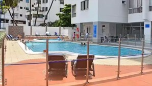 En swimmingpool med solstolar och ett staket, omgiven av byggnader.