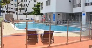A swimming pool with lounge chairs and a fence, surrounded by buildings. - CARTAGENA-Vista al Laguito 🌅 | Remodeled | VRBO Ready | Steps from the beach. (Cartagena de Indias)