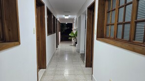 Un corridoio con porte e finestre in legno, pavimento piastrellato e una pianta in vaso.