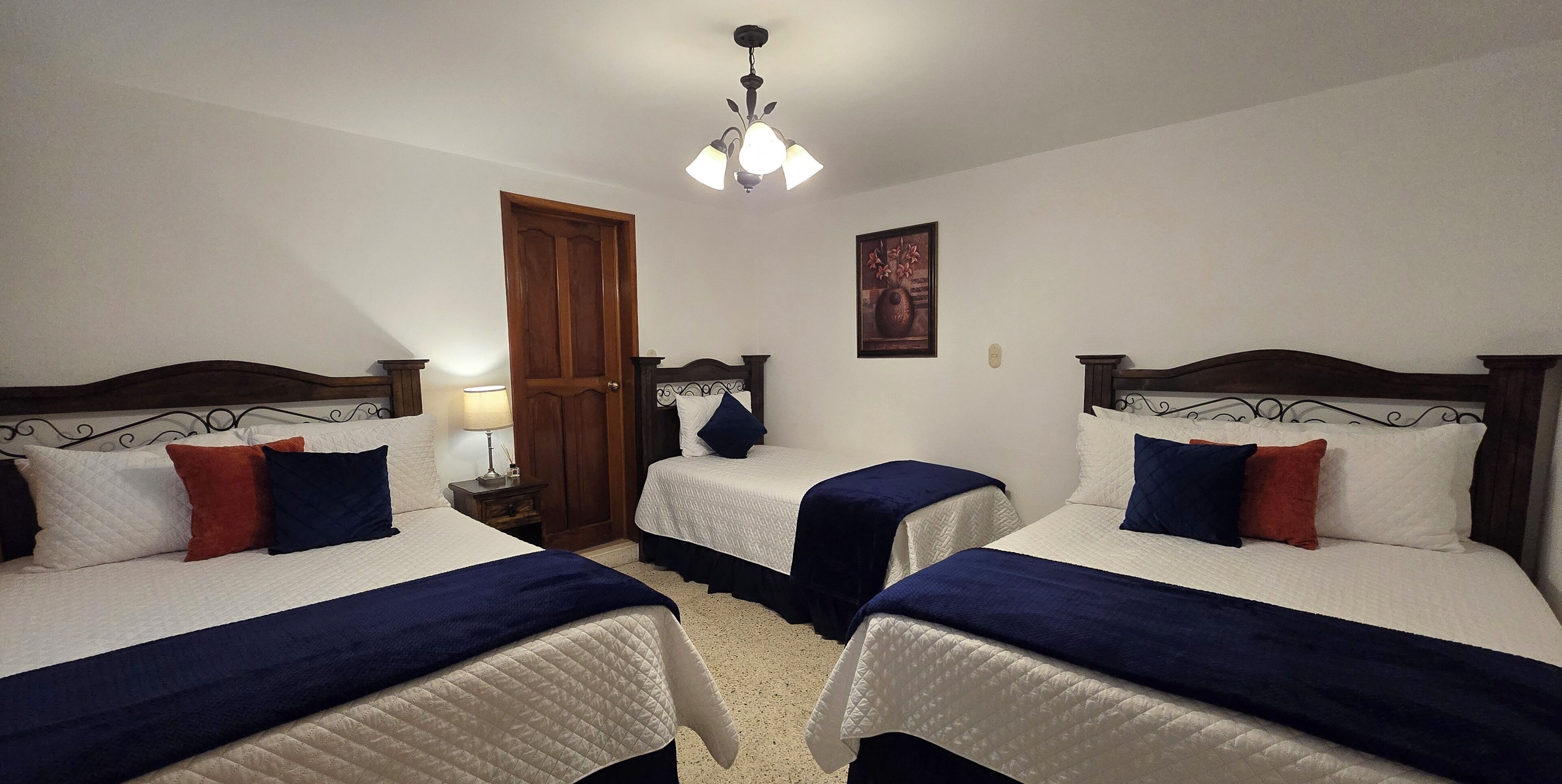 Habitación de hotel con dos camas, una puerta de madera, un cuadro en la pared y una lámpara en el techo.