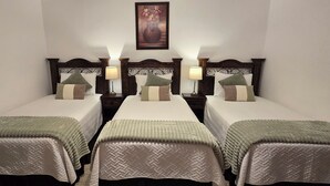 Una camera d'albergo con tre letti singoli, ognuno con una coperta verde e cuscini bianchi. Sono presenti comodini con lampade e un quadro appeso alla parete sopra i letti.