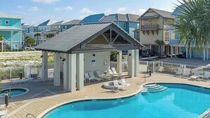 Piscina com espreguiçadeiras, um pequeno pavilhão e vista para a praia.