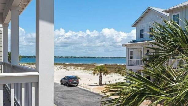 Vista costeira com praia, um carro estacionado e um edifício com varanda.