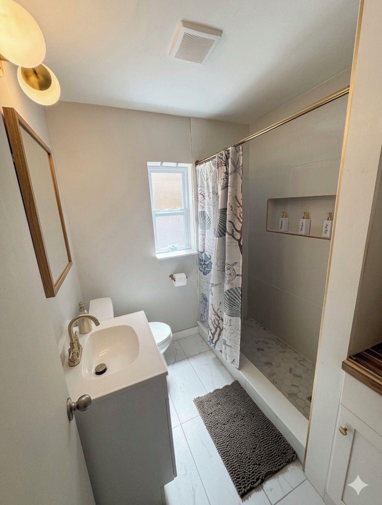 A bathroom with a toilet, sink, shower, and a window.