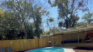Un cortile con piscina, recinzione in legno e alberi.