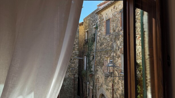 A room with a window overlooking a narrow street with old buildings and a lamp post.