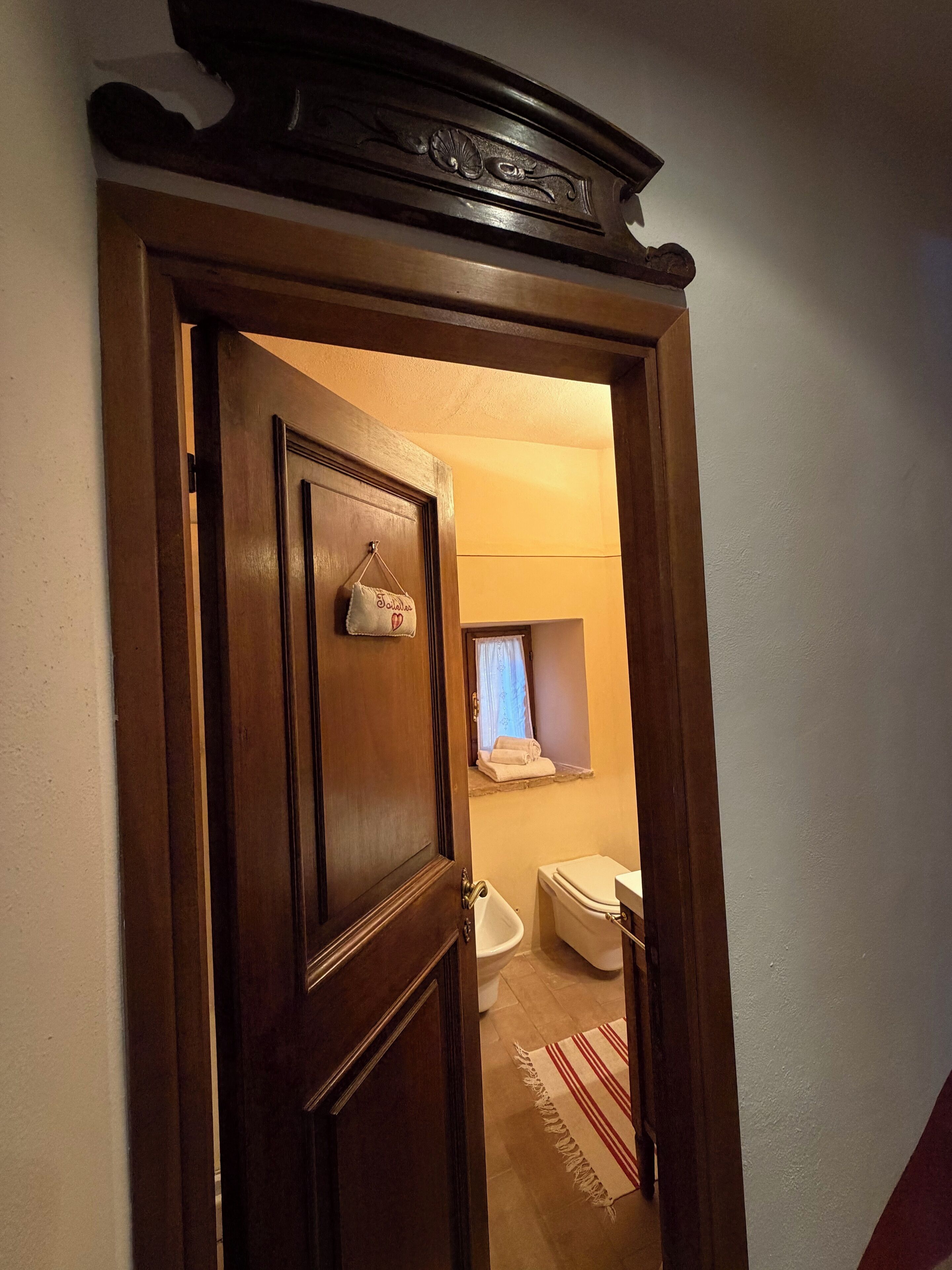 Puerta de madera que da a un baño con inodoro, bidé y un perchero para toallas.