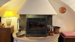 A stone fireplace with a chimney, a wooden table with a lamp, and rustic kitchen utensils.