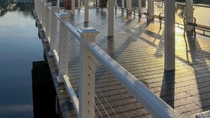 Een overdekte doorgang met banken, een leuning en een rustig waterlichaam op de achtergrond.