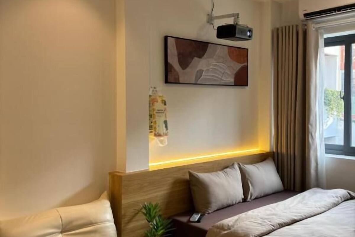 Habitación de hotel con cama, sofá, proyector montado en la pared y ventana con cortinas.