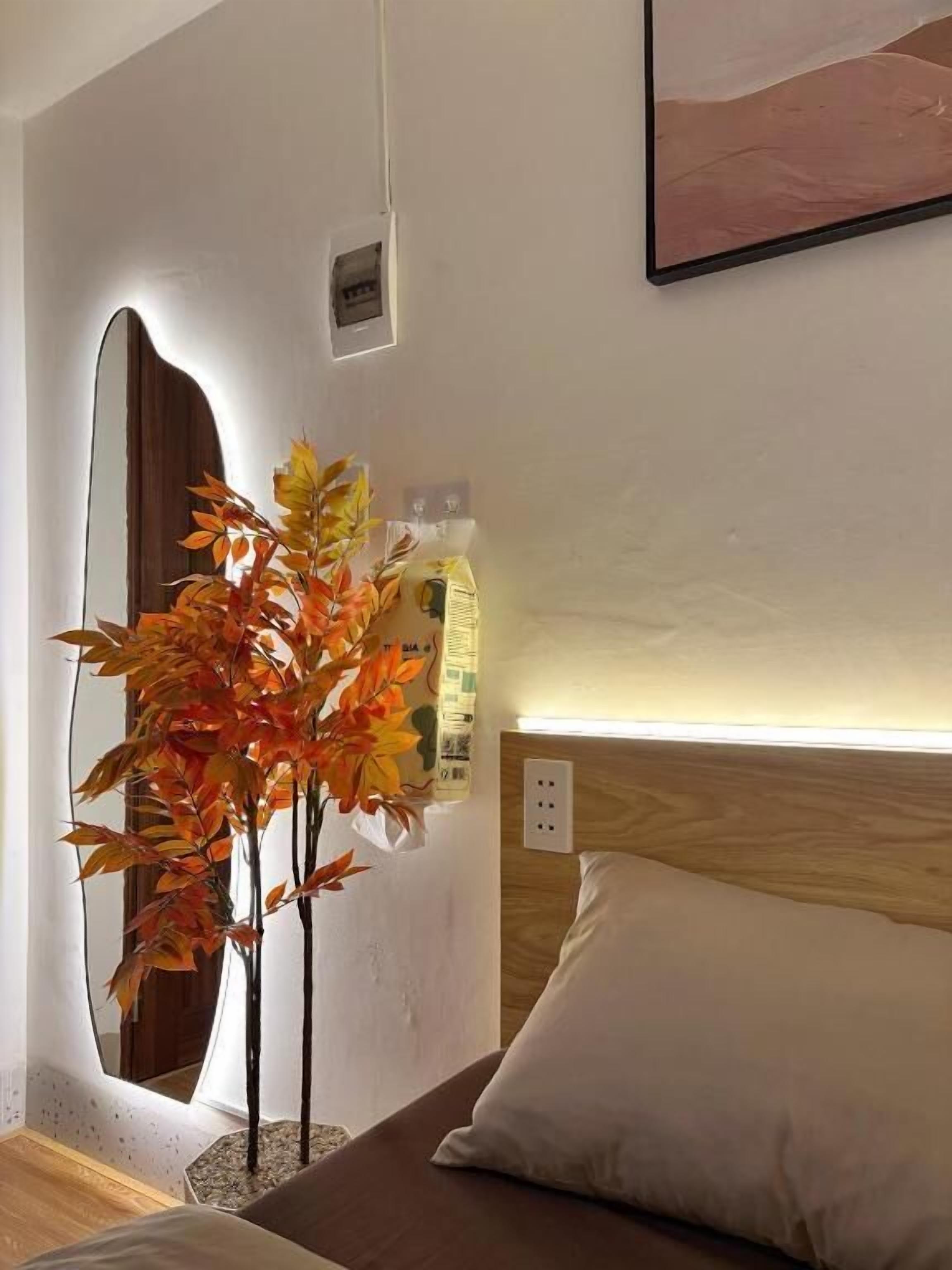 A bedroom with a bed, a nightstand, a mirror, and a wall-mounted power outlet.