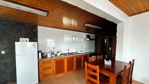 A kitchen with wooden cabinets, a white refrigerator, a microwave, and a dining table with chairs. - Retiro dos Cabritos (Madalena)