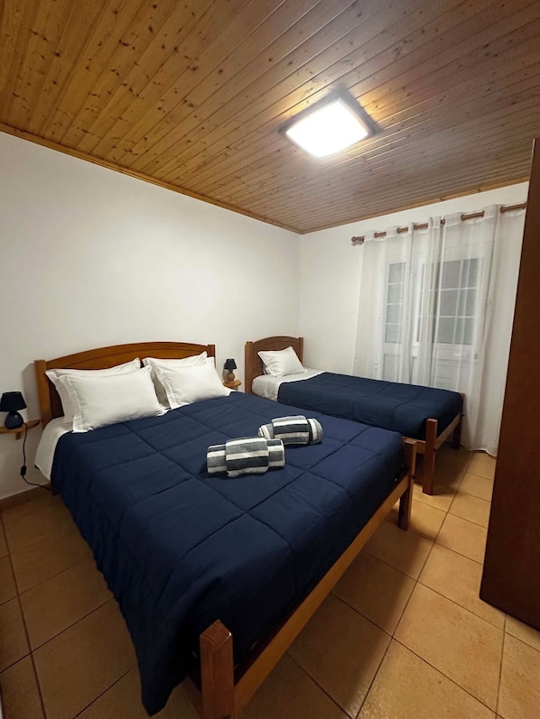 A room with two wooden beds, a ceiling light, and a window with curtains.