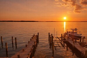 Eine Holzstege, der sich in ruhiges Wasser erstreckt, mit einem Sonnenuntergang im Hintergrund.