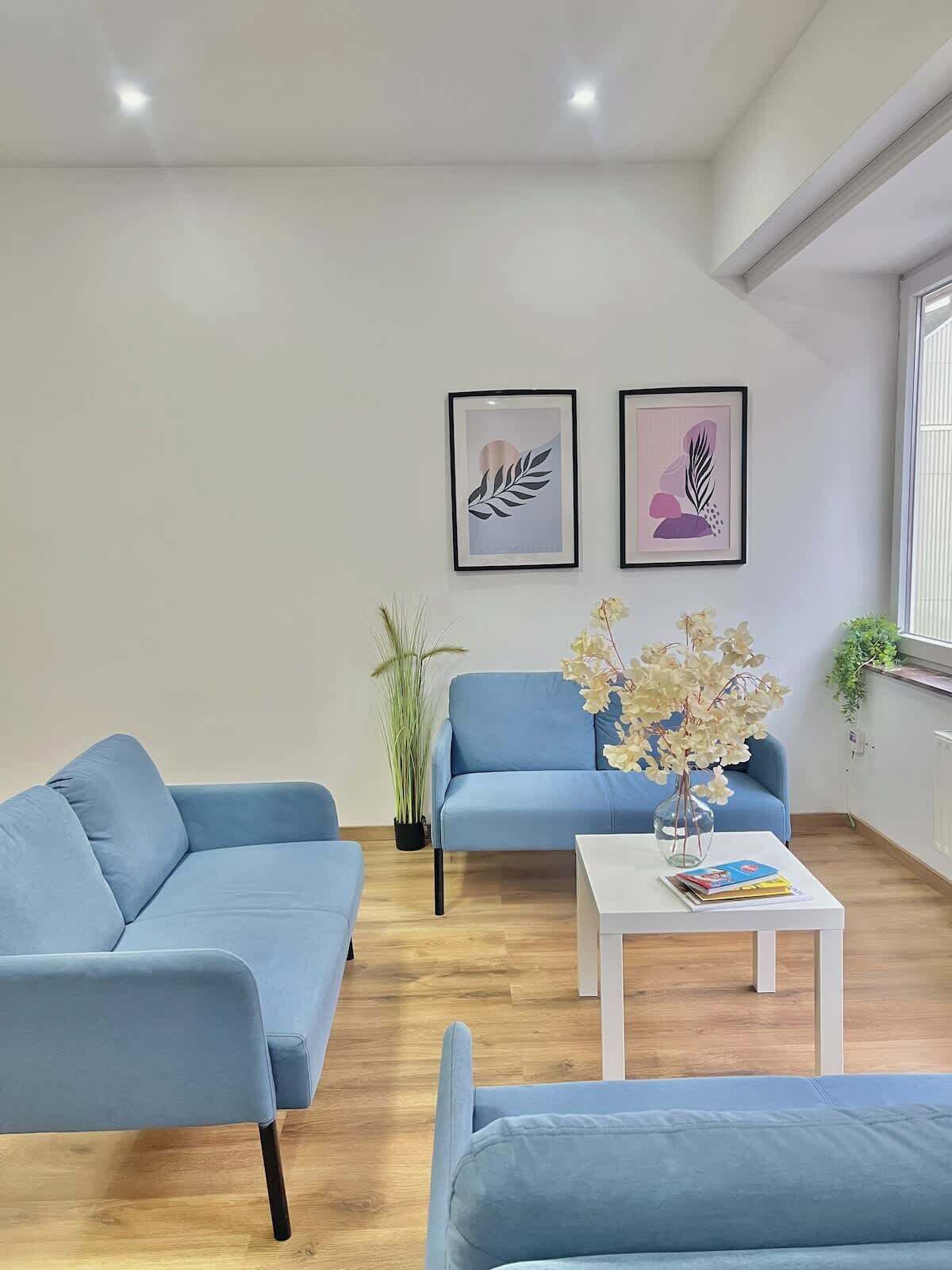 Un salon moderne avec deux canapés bleus, une table basse blanche et deux œuvres d’art encadrées accrochées au mur.