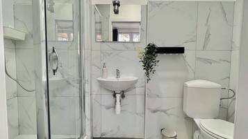 Une salle de bain avec une douche à parois de verre, un lavabo, des toilettes et une petite poubelle.