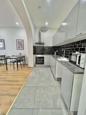 Una cocina moderna con gabinetes grises, un salpicadero de baldosas negras, un microondas y un comedor con mesa y sillas.