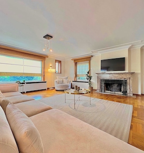 A spacious living room with a large sofa, a fireplace, a television, and a view of the outdoors.