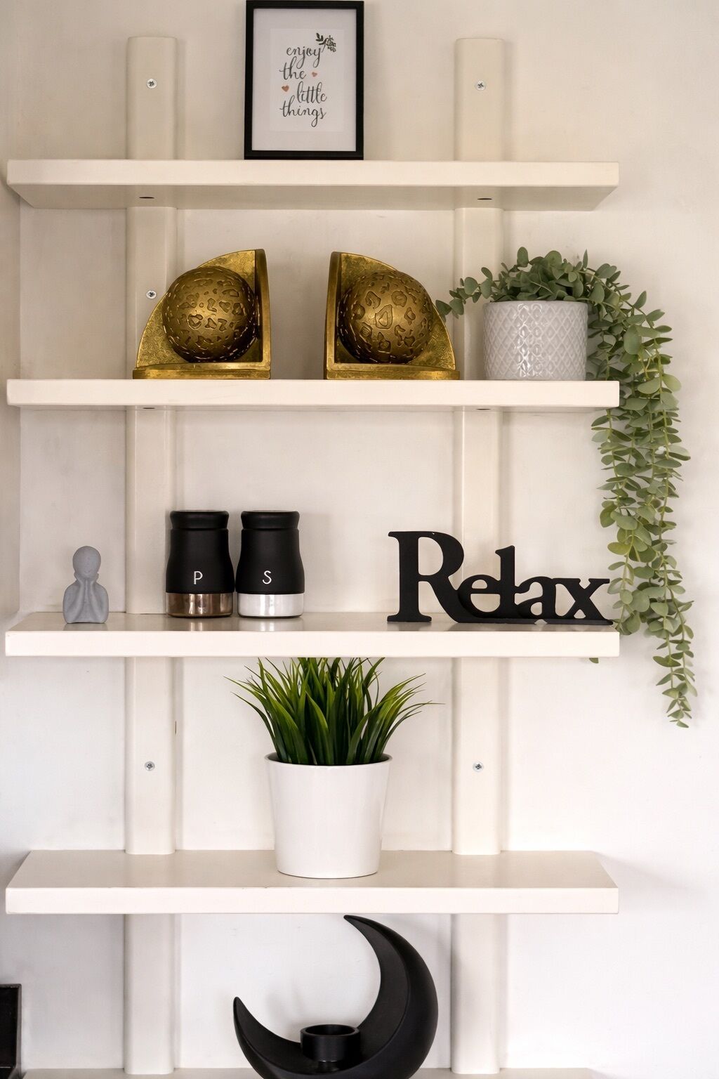 A wall-mounted shelf with decorative items, including two golden spherical objects, a potted plant, and a framed inspirational quote.