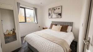 Une chambre à coucher avec un grand lit, une fenêtre, une table de chevet et une œuvre d’art accrochée au mur.
