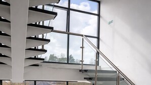 Un escalier moderne avec des rampes en verre, offrant une vue sur une rivière et des bâtiments à l’extérieur.