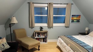 Un dormitorio con cama, una silla, una estantería y una ventana con cortinas.