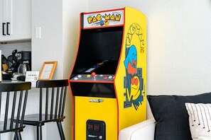Pac-Man-peliautomaatti huoneessa, jossa on ruokapöytä, tuoleja ja sohva.