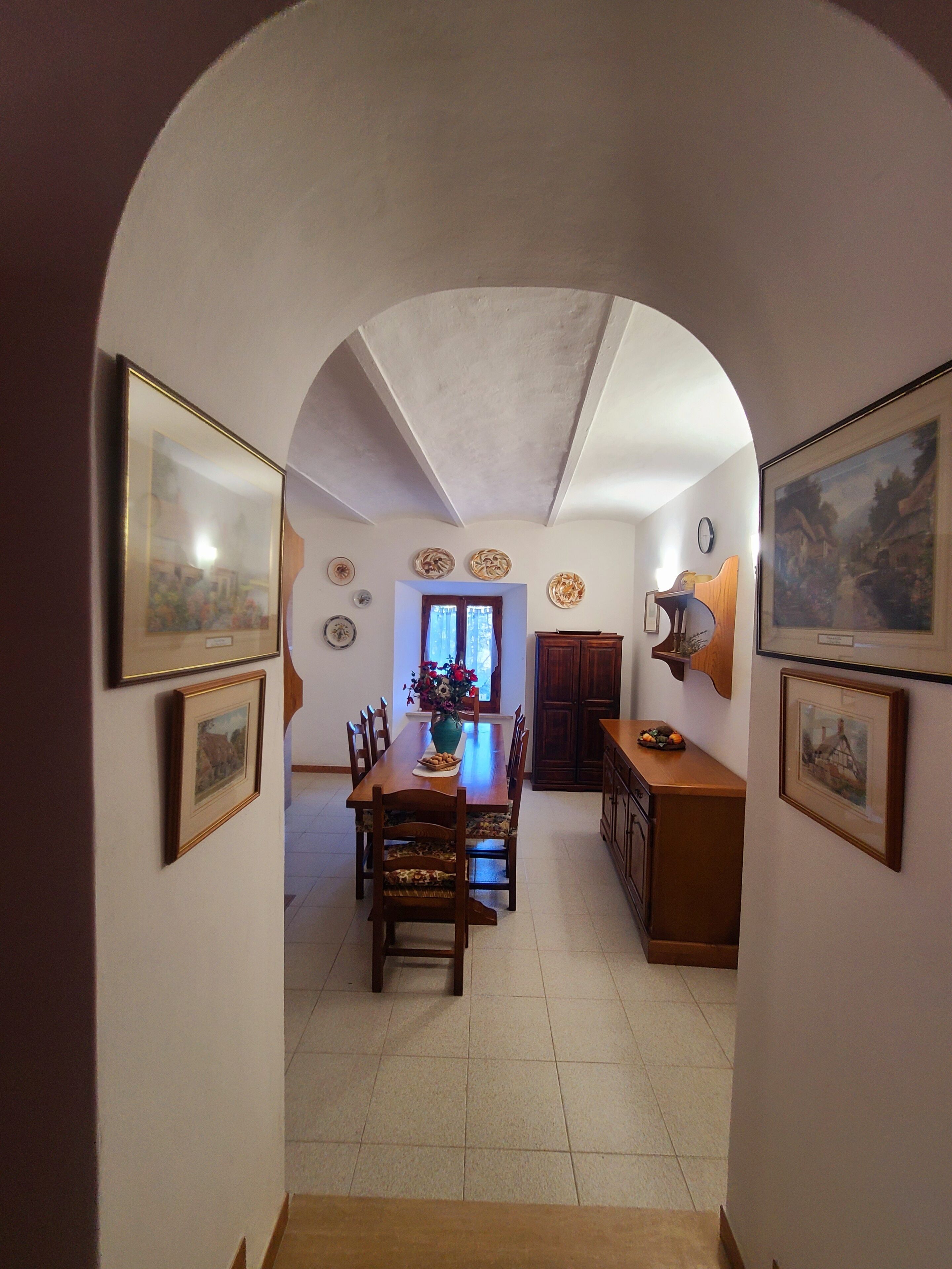 An arched hallway leading to a dining area with a table, chairs, and a vase of flowers.