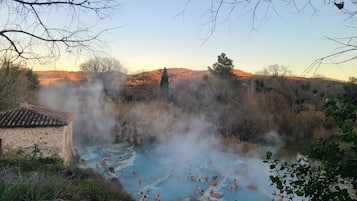 A natural hot spring with people bathing, surrounded by trees and hills.