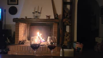 A fireplace with burning logs, two glasses of red wine, and a brick mantelpiece.