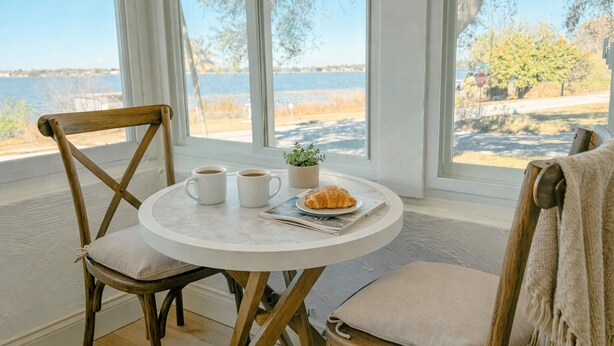Une table ronde avec deux tasses blanches, un croissant et une petite plante.