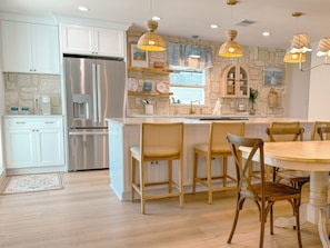 A modern kitchen with white cabinets, a stainless steel refrigerator, a stone accent wall, and a dining area with wooden chairs and a round table.