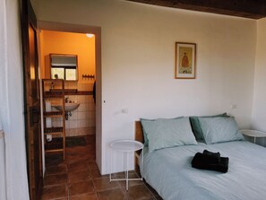 Ein Schlafzimmer mit Bett, Nachttisch, kleinem Tisch, Bad mit Waschbecken und Spiegel sowie einer Treppe zu einer oberen Ebene.