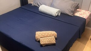 Een bed met een donkerblauwe spreidek, twee opgerolde handdoeken en een kussen met een bloemenprint.