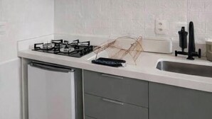 Een keuken met een gasfornuis, een magnetron, een vaatwasser en grijze kastjes.