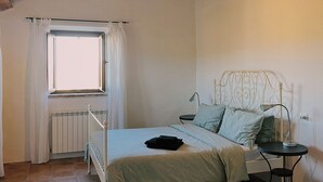 A bedroom with a wooden ceiling, a bed with a metal headboard, a small bedside table, and a window with curtains. - Casale Milleluci - double apartment in the countryside 10 min from the sea (SENIGALLIA)
