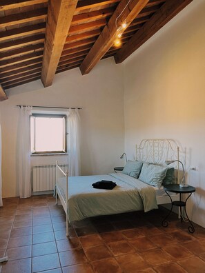 Ein Schlafzimmer mit Holzboden, einem Bett mit Metallkopfteil, einem kleinen Nachttisch und einem Fenster mit Vorhängen.