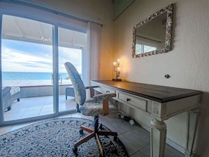 A room with a large sliding glass door leading to a balcony with a view of the ocean. There is a desk with drawers and a mirror on the wall. - Once Upon a Tide | Oceanfront + Sleeps 8 (Playa Encanto)