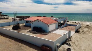 A beachfront property with a covered patio, a small building with a red roof, and a view of the ocean. - Once Upon a Tide | Oceanfront + Sleeps 8 (Playa Encanto)