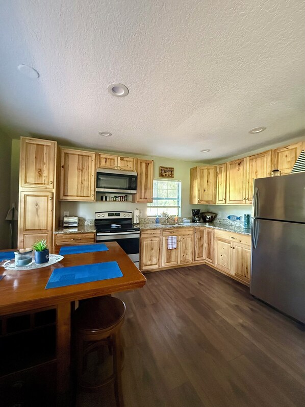 A kitchen with wooden cabinets, a stainless steel refrigerator, a microwave, and a stove.
